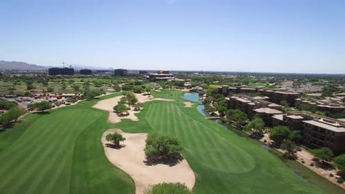 Aerial fly down a golf course's adjacent fairways toward two golf carts in the distance, Scottsdale,
