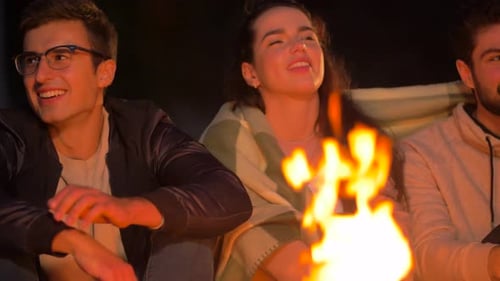 Friends sharing stories and warming themselves at a campfire on a summer night