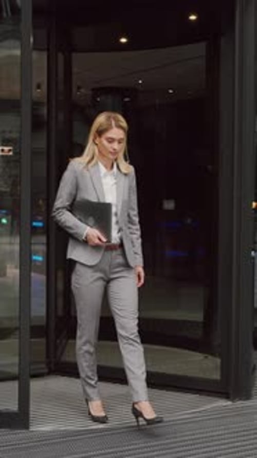 Mulher com laptop saindo do escritório através de portas deslizantes