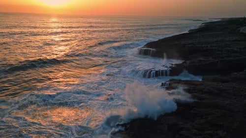 Picturesque ocean sunrise foamy waves lapping rocky coastline aerial view