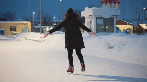 Woman Ice Skating in Snowy Winter Park at Night