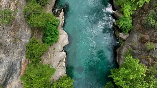 Vue aérienne d'une rivière turquoise coulant entre des falaises rocheuses et un feuillage vert luxuriant