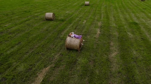 Relaxing in Nature Woman Seated on a Hay Bale in a Lush Field Smiling Beneath the Clear Sky