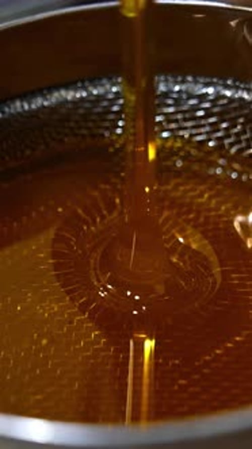 Organic fresh honey pouring on the metal sieve. Filtering honey right after extraction.