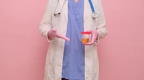 Doctor hand holds a container for taking a urine test for virus, studio pink background. Hand in a m