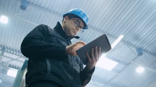 Ein Fabrikarbeiter mit Schutzhelm benutzt einen Tablet-Computer.