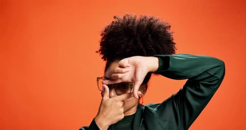 Young Person Dances with Finger Frame on Orange