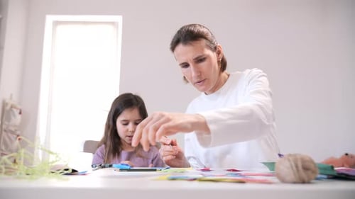 Mother and Young Daughter Sitting at a Table Designing and Making Colorful Paper Crafts Focusing on