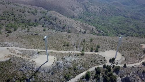 Aerial footage of Wind turbines spinning, in a mountain forest surrounding