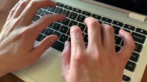 Hände tippen auf einem Laptop mit natürlichem Licht, das aus dem Bürofenster hereinkommt.