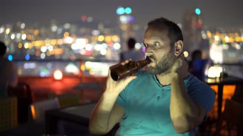 Pensive Man Drinking Beer at Night Rooftop Bar