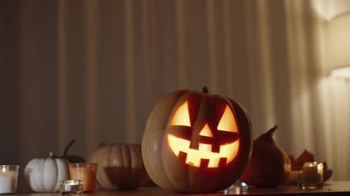 Pumpkins on the Table, with a Large Jack-o'-Lantern at the Center with a Flame Inside. Curtains