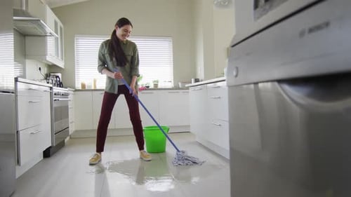 Happy caucasian woman cleaning floor with mop and bucket of water at home