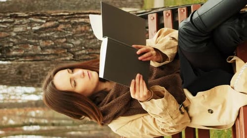 Woman turning pages and reading book in autumn city park. Vertical video