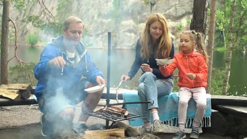 A Couple with a Child Grilling in the Forest on the Shore of the Lake