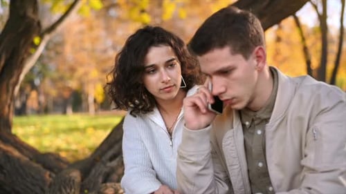 A romantic couple in an autumn park. Man is talking on the phone. Autumn atmosphere, yellowed trees