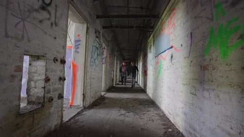 Two People Walking in a Graffiti-Filled Abandoned Corridor