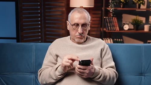 Senior Man Using Smartphone on Couch Indoors