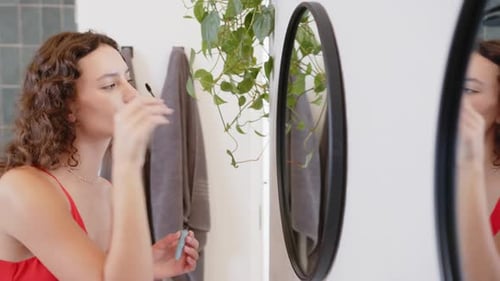 Applying makeup, woman looking in mirror in home setting, relaxing