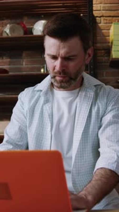 Man Works on Orange Laptop at Kitchen Table