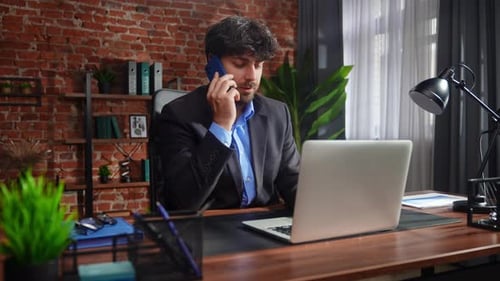 Businessman in Office Talking on Phone and Using Laptop