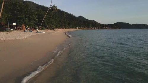 low angle forward dolly shot of ocean and beach with kayak and sups with man walking into ocean on a
