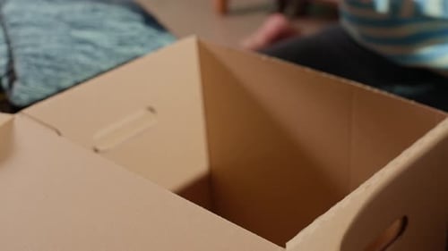 Frau hält Spendenbox mit Kleidung auf dem Bett