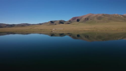 Rotating epic drone shot out on top of the Song-Kol lake looking at the small yurt village in Kyrgyz