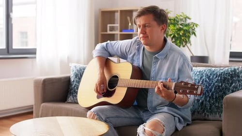 Man Playing Acoustic Guitar on Sofa in Living Room