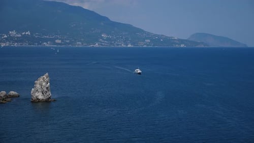 The Sea and a Yacht Floating on the Water Against the Background of Mountains
