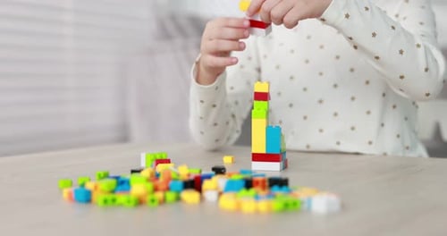 Kleines Mädchen spielt drinnen mit bunten Bausteinen am Holztisch, Nahaufnahme