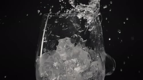 Clear ice cubes and splashed water pouring in transparent wineglass slow motion