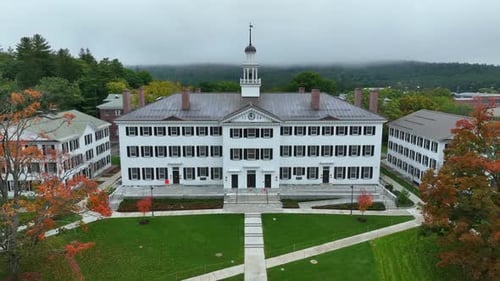 Aerial drone videography of large white academic building on a overcast fall day. Sidewalks provide