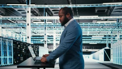 Technician at Server Hub Workspace Desk Using Laptop to Do Maintenance Tasks