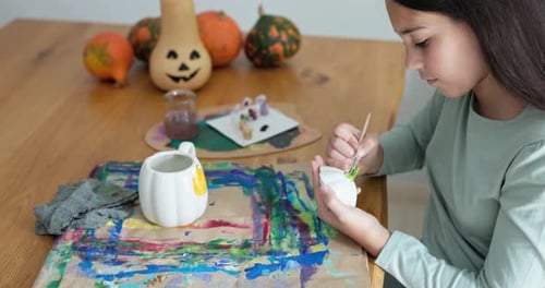 Young girl painting pumpkin cup for Halloween party - Holiday, childhood and autumn lifestyle