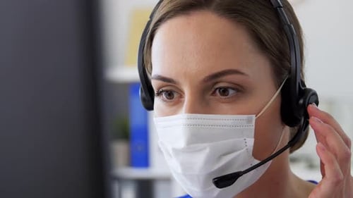 Hispanic female doctor wearing face mask works at hospital on computer with headset