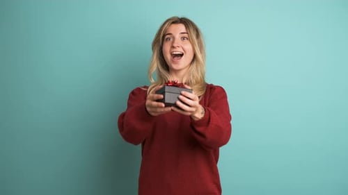 Happy Young Woman Receiving Gift Box in Blue Studio