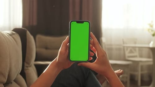 Woman Lying on Sofa with Modern Smartphone in Hand While Looking on Mock Up Screen Concept of Green