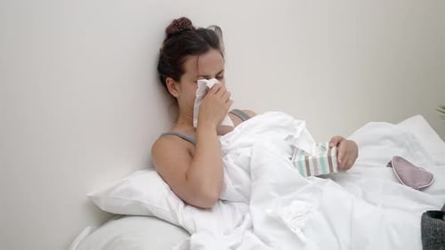 Luttant contre la maladie, elle est assise dans son lit, le nez tamponné avec des mouchoirs contenant des gouttes médicales
