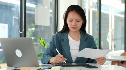 Uma mulher está sentada em uma mesa com um laptop e um tablet
