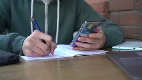 Boy with Smartphone and Notepad Doing Homework by Table in Cafe Adolescent