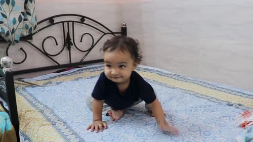cute toddler baby boy trying to stand for the first time at bed at home