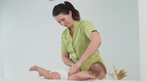 Side View of Smiling Female Masseuse Doing Massage on Healthy Infant Baby Lying on Table Small