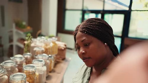Woman Inspects Jars of Pasta at a Food Market