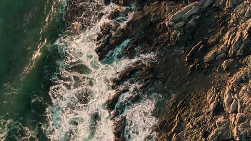 Drone top down crane shot of breaking waves on rocky Costa Rica beach in sunset