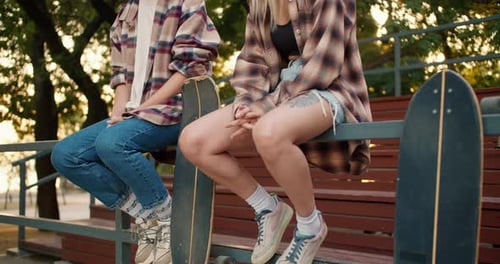 Closeup Shot of Two Girls Sitting in Plaid Shirts with Their Skateboards Near a Skate Park and