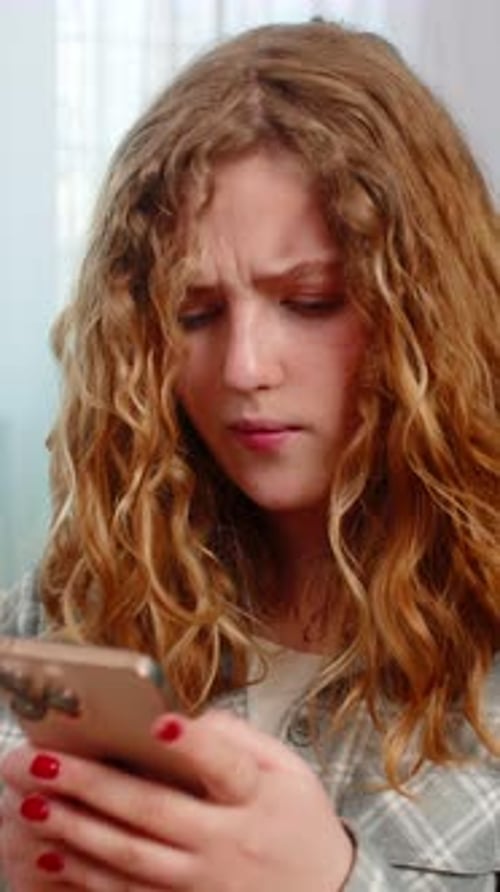 Junge Frau sitzt auf dem Sofa und schreibt wütend eine SMS und winkt mit der Hand, verärgert über eine Nachricht im Handy-Chat