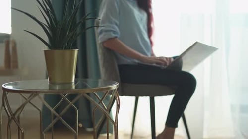 A Woman is Diligently Working on Her Laptop in the Comfort of Her Home Surrounded By a Vibrant