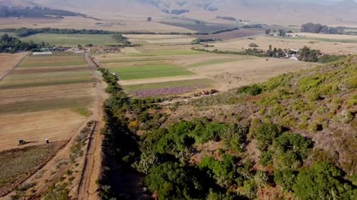 Drone shot over hill with farm land and hills in the background.