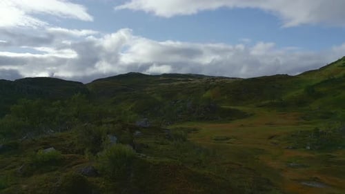 A drone soars over a picturesque hilly landscape, where a winding creek flows gently through vibrant